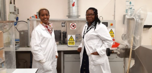 two women in white lab coats in a laboratory smiling at the camera